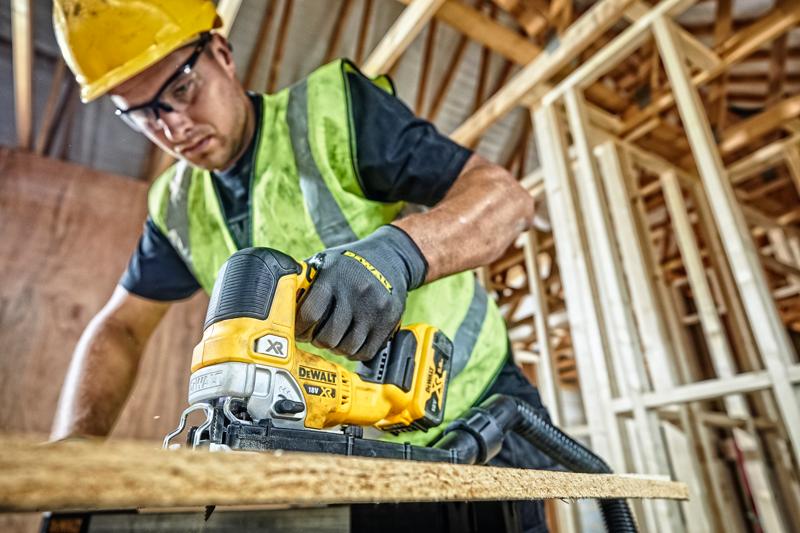 DEWALT DCS334P2 Stichsäge schneidet Holz auf Baustelle, bedient von Arbeiter mit Sicherheitsausrüstung.